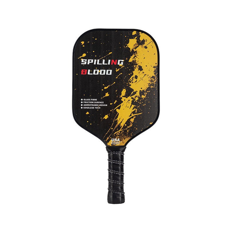 Xephira 16mm defensive paddle on a black background with yellow and red paint splatter, a bold design. This fiberglass paddle, showcasing what material is best for pickleball paddles, is suitable for players focused on control and stability.