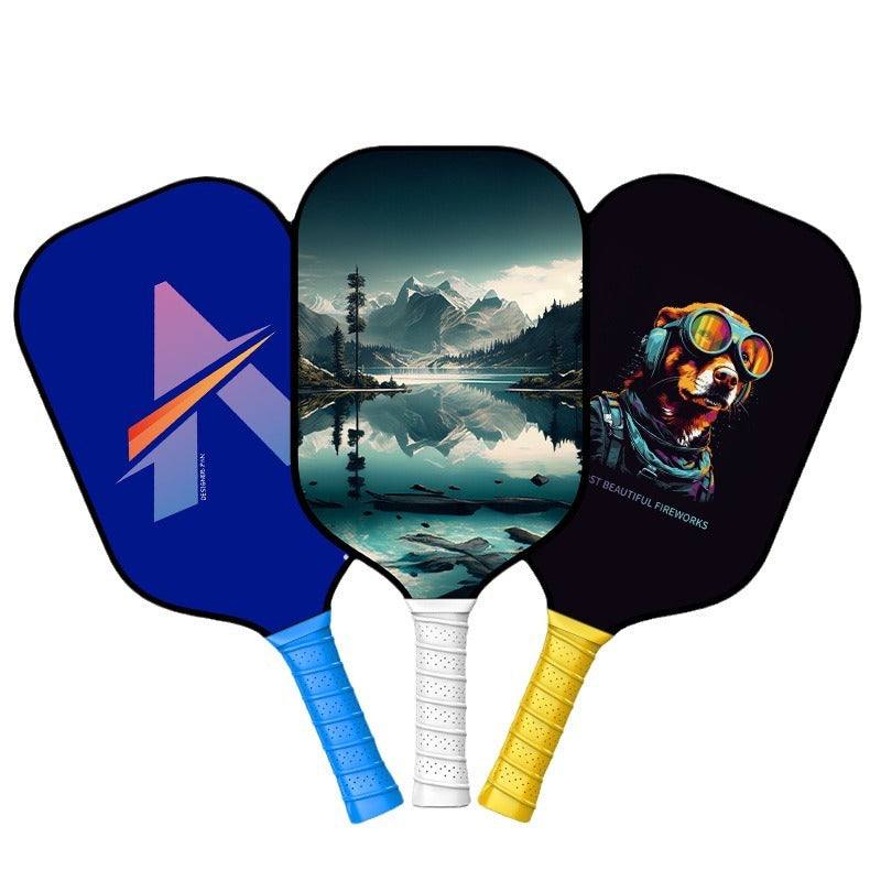 Three carbon fiber pickleball paddles with different designs (Abstract 'A', Mountain/Lake, and Cartoon Dog), featuring blue, white, and yellow grips. The USP designs are ideal for users asking where to buy a pickleball paddle that stands out