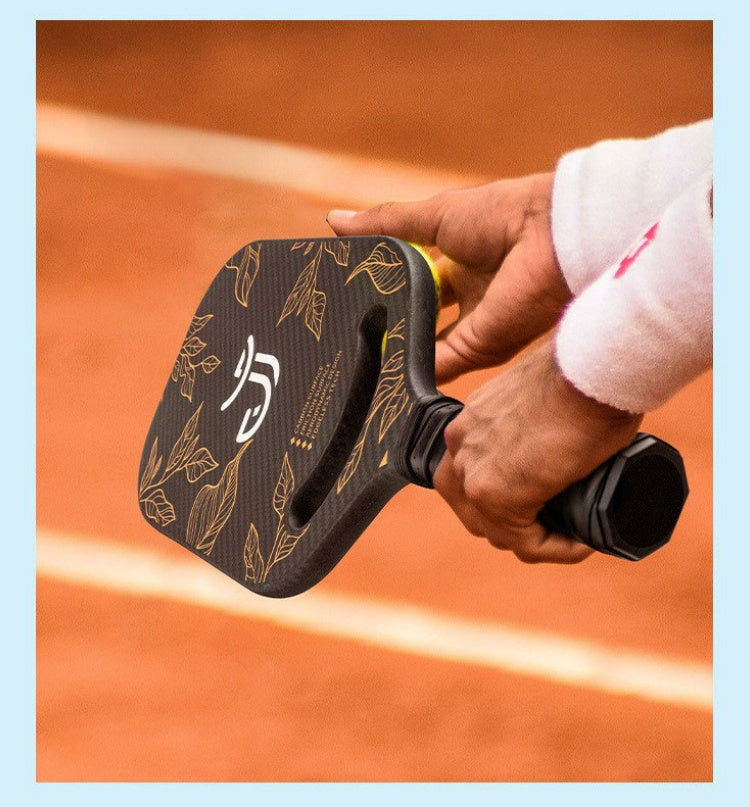 Close-up shot showing a player holding the dark, gold leaf patterned pickleball paddle with two hands. This highlights the importance of the correct grip: how to hold a pickleball paddle.